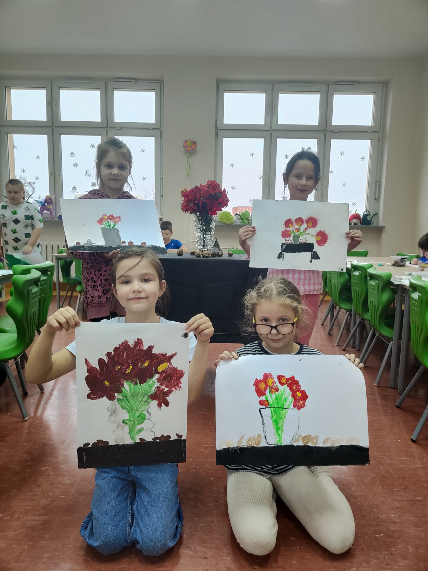 Dziewczynki trzymają w ręku obraz namalowanych kwiatów.